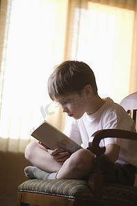 男孩盘腿坐在椅子上看书