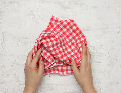 两只女手拿着白桌上皱巴巴的白红方格纺织厨房餐巾
