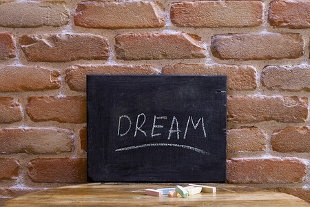 在砖墙背景的木桌上，用手淹没了带有 DREAM 字样的黑板