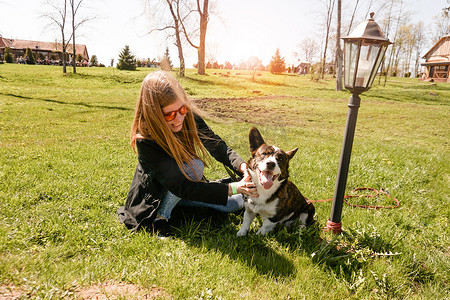 戴着红色太阳镜的年轻女人在夏日的绿色草坪上和她的柯基犬玩耍