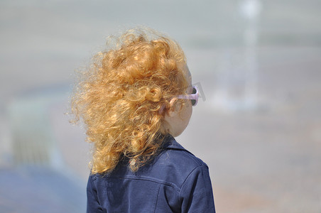 红发摄影照片_一个阳光明媚的日子，在街上飘扬着头发的红发女孩。
