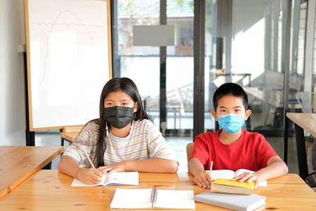 学生写做作业摄影照片_女孩男孩学生戴着口罩学习写笔记做作业。