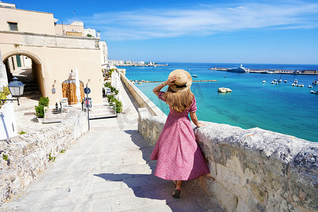 戴着帽子的美丽年轻女子沿着奥特朗托古城墙漫步，欣赏意大利萨兰托奥特朗托村的壮丽全景