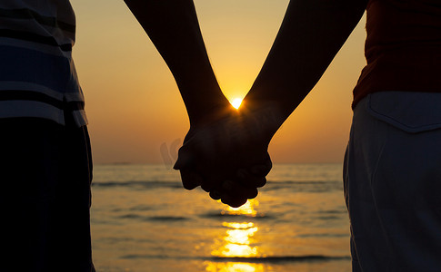 海滩情侣摄影照片_夕阳下手牵手的情侣剪影。