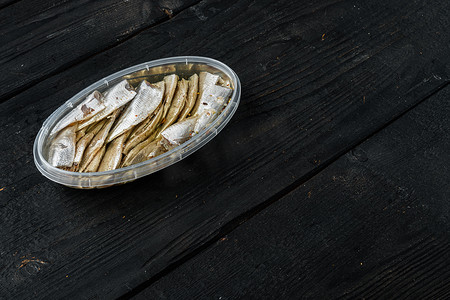 腌咸凤尾鱼片，在塑料容器中，在黑色木桌背景上，有复制空间和文本空间