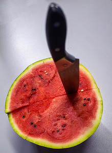 一把大刀插在一个成熟的红西瓜里，我们将把它缝在灰色的桌子上。