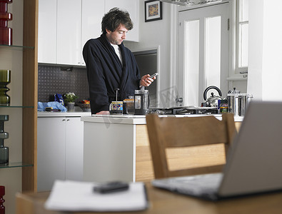 男人站在厨房里，前景是桌子上的短信笔记本电脑