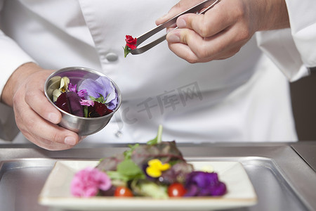 男厨师在商业厨房沙拉上安排食用花卉的中段特写