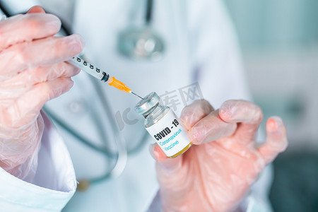 身穿制服和戴面罩的手套的医生或护士在实验室拿着带有 COVID-19 冠状病毒疫苗标签的药瓶疫苗瓶