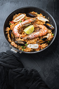 西班牙菜摄影照片_海鲜饭传统西班牙菜在煎锅中供应，黑色纹理表面