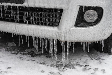 冰雪覆盖的汽车保险杠与冰柱关闭，欧洲冻雨后的车辆停车安全