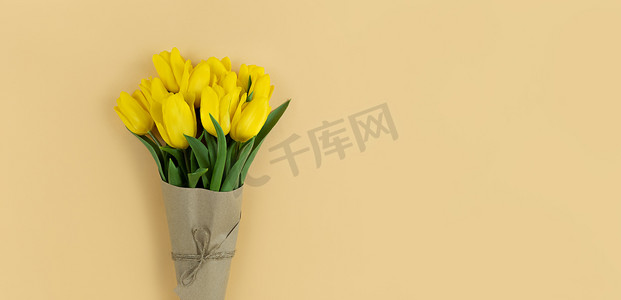 黄色郁金香花束包裹在米色背景的牛皮纸中，带有复制空间。