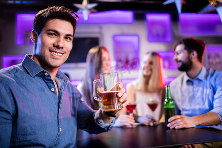在酒吧柜台喝啤酒的年轻微笑男子的画像