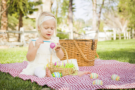 可爱的小女孩在野餐毯上给复活节彩蛋上色