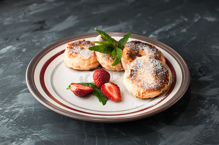 美食早餐-凝乳煎饼、芝士蛋糕、凝乳煎饼、草莓、薄荷和糖粉放在白盘子里。