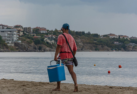 保加利亚索佐波尔 — 09/06/2018: 一个穿着红色 T 恤和蓝色盒子的男人沿着海滩散步