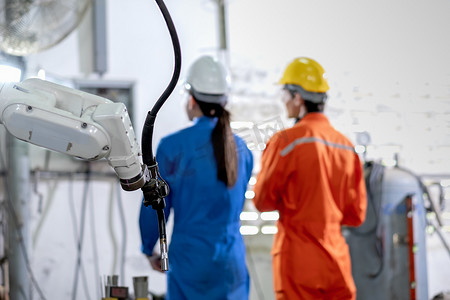 工厂机器人机器在工作区的背景下与工人一起监控电气系统。
