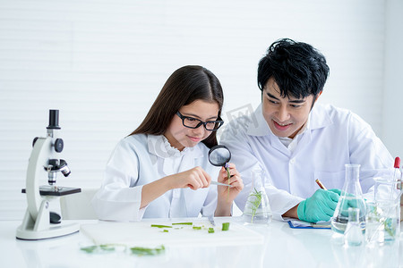 年轻的白人科学家女童用镊子夹住一朵花，用放大镜和亚洲教师指南查看更多细节，以便在实验室或课堂上进行分析。