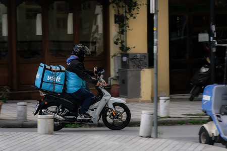 塞萨洛尼基，希腊 Wolt 食品快递员骑着摩托车在城市道路上飞驰。