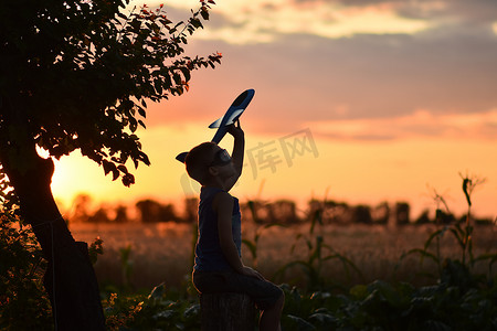 飞机夕阳摄影照片_日落时分，一名带飞机的儿童飞行员在街上玩耍。