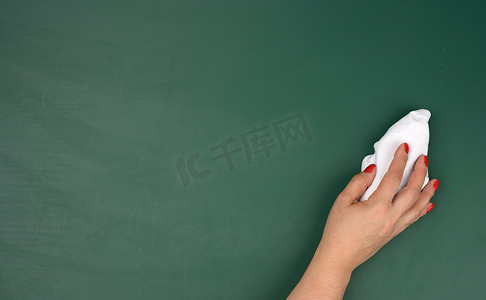 一个女人的手拿着一块白色的旧布，背景是绿色粉笔板