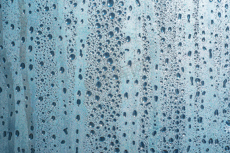 闪闪发光摄影照片_雨天玻璃上的雨滴。玻璃上闪闪发光的水面。水滴呈球状或球状。蓝色雨滴背景。