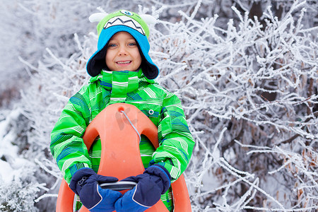 在冬季公园玩雪橇的小男孩