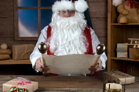 圣诞老人坐在他的工作室里，读着一本写着他的顽皮和好人名单的书