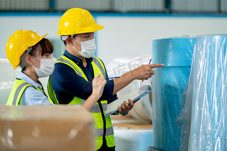 两名穿着安全制服的工厂工人男女在仓库中一起工作，检查产品并在工业企业的收集和转移过程中进行讨论。