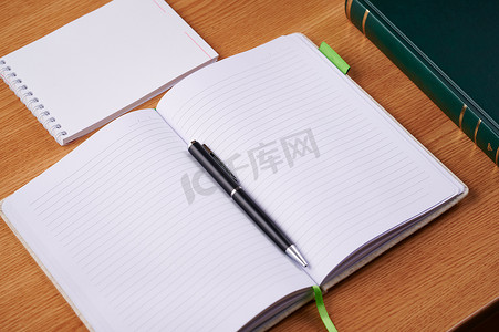 书放在桌子上摄影照片_普通空白打开的笔记本，里面有一叠钢笔，里面的容器放在桌子上。