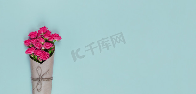 小玫瑰摄影照片_蓝色背景上用牛皮纸包裹的小花粉色玫瑰花束，带有复制空间。