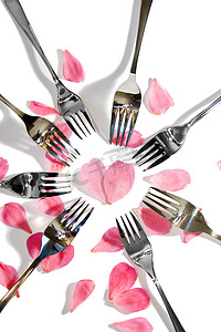 心形的花瓣摄影照片_围绕心形的金叉和银叉与玫瑰花瓣