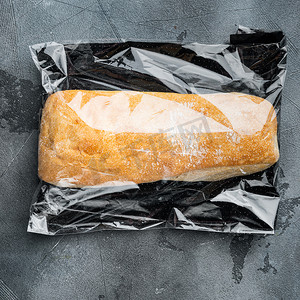 灰色背景条摄影照片_一条新鲜烘焙的工匠全麦 ciabatta 面包放在市场袋子里，灰色背景，顶视图平铺