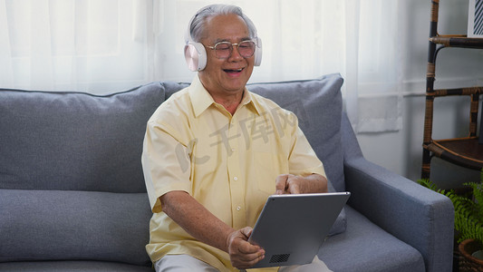 老人祖父微笑放松戴耳机正在使用数字平板电脑听音乐