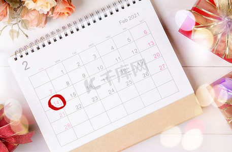 日历和花与备忘录 2 月 14 日情人节在桌子上有模糊的散景背景，提醒爱情惊喜，浪漫和甜蜜，庆祝和装饰，顶视图，假日概念。