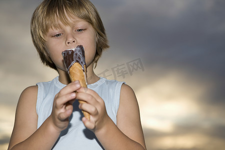 身穿背心的金发 7-8 岁男孩手里拿着融化的巧克力冰淇淋