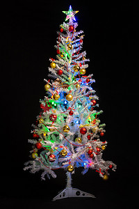 圣诞树亮摄影照片_黑色背景中喜庆装饰的人造白色圣诞树