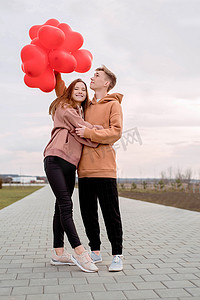 年轻的情侣带着红气球在户外拥抱玩得开心