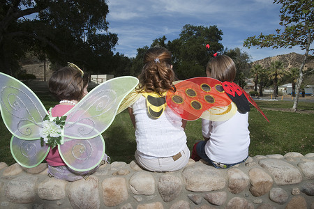 三个女孩 (7-12) 穿着戏服坐在公园里