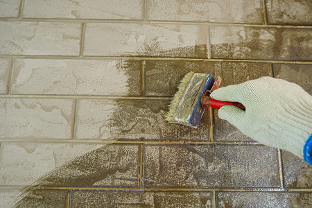 砖摄影照片_一名建筑工人在砖墙上涂漆。画家用刷子在墙壁上涂底漆，在房子或房间里进行维修。重建建筑，专家修复墙壁