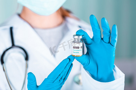 戴手套的护士摄影照片_女医生或护士穿着制服和戴面罩的手套在实验室拿着带有 COVID-19 冠状病毒疫苗标签的药瓶疫苗瓶
