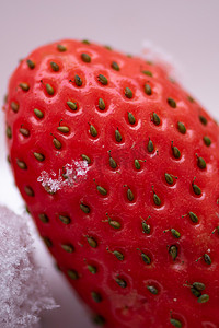 红草莓摄影照片_白色背景下成熟红草莓种子及其上的一块冰的宏观观察