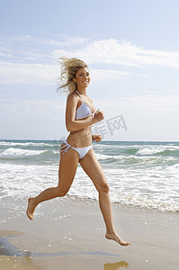 在海滩上奔跑的快乐年轻女子的全长肖像