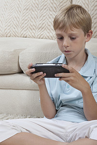 男孩盘腿坐着便携式游戏机