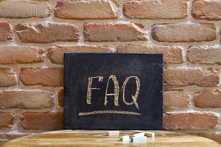 木摄影照片_在砖墙背景的木桌上，用手淹没了带有 FAQ 字样的黑板。