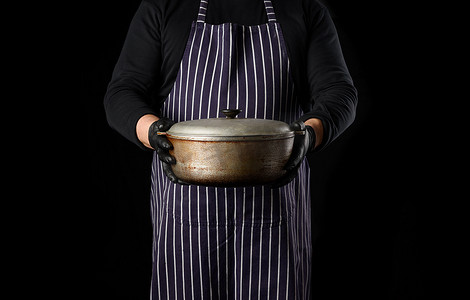一条条纹围裙的男厨师拿着一个带盖的铝锅