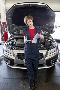 打开引擎盖摄影照片_年轻的女机械师在车库里看纸，汽车打开引擎盖
