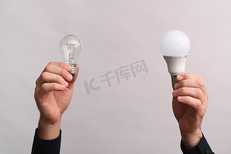 在男性手中，一个 LED 灯和一个白炽灯泡。