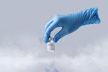 疫苗蓝色摄影照片_手拿着 Covid-19 的冷冻冷疫苗瓶。