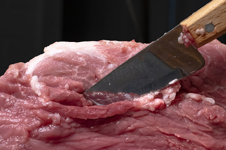 烤羊肉串摄影照片_在特写镜头中用刀将猪肉或牛肉切成薄片。肉类菜肴和食品的准备。烤羊肉串、烧烤或烤肉串用的红肉片。用刀切生鲜肉。食谱